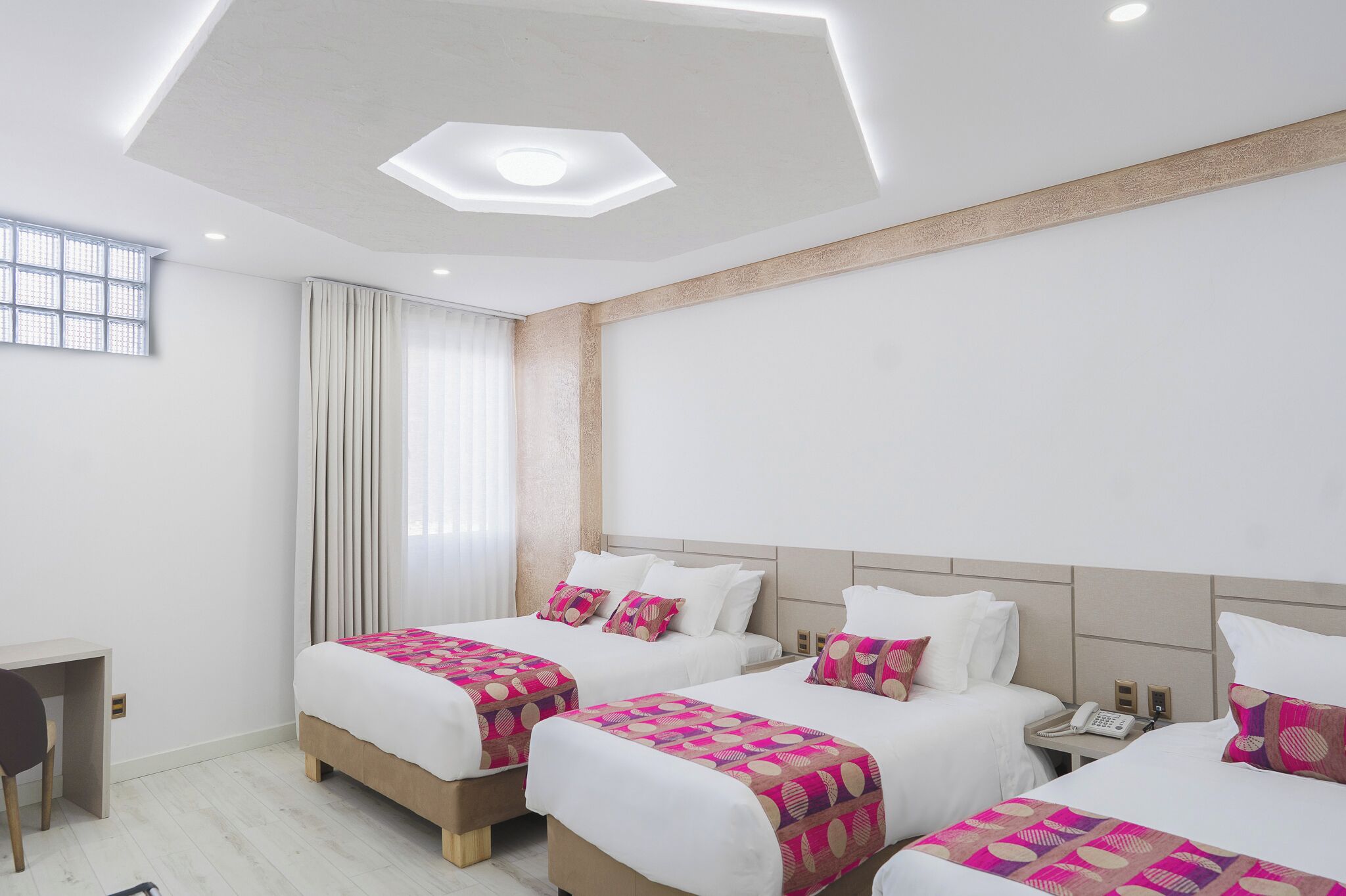 A hotel room with three beds, a desk, and a window with curtains.