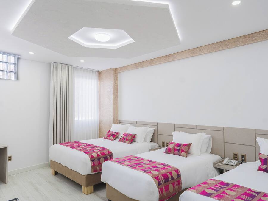A hotel room with three beds, a desk, and a window with curtains.