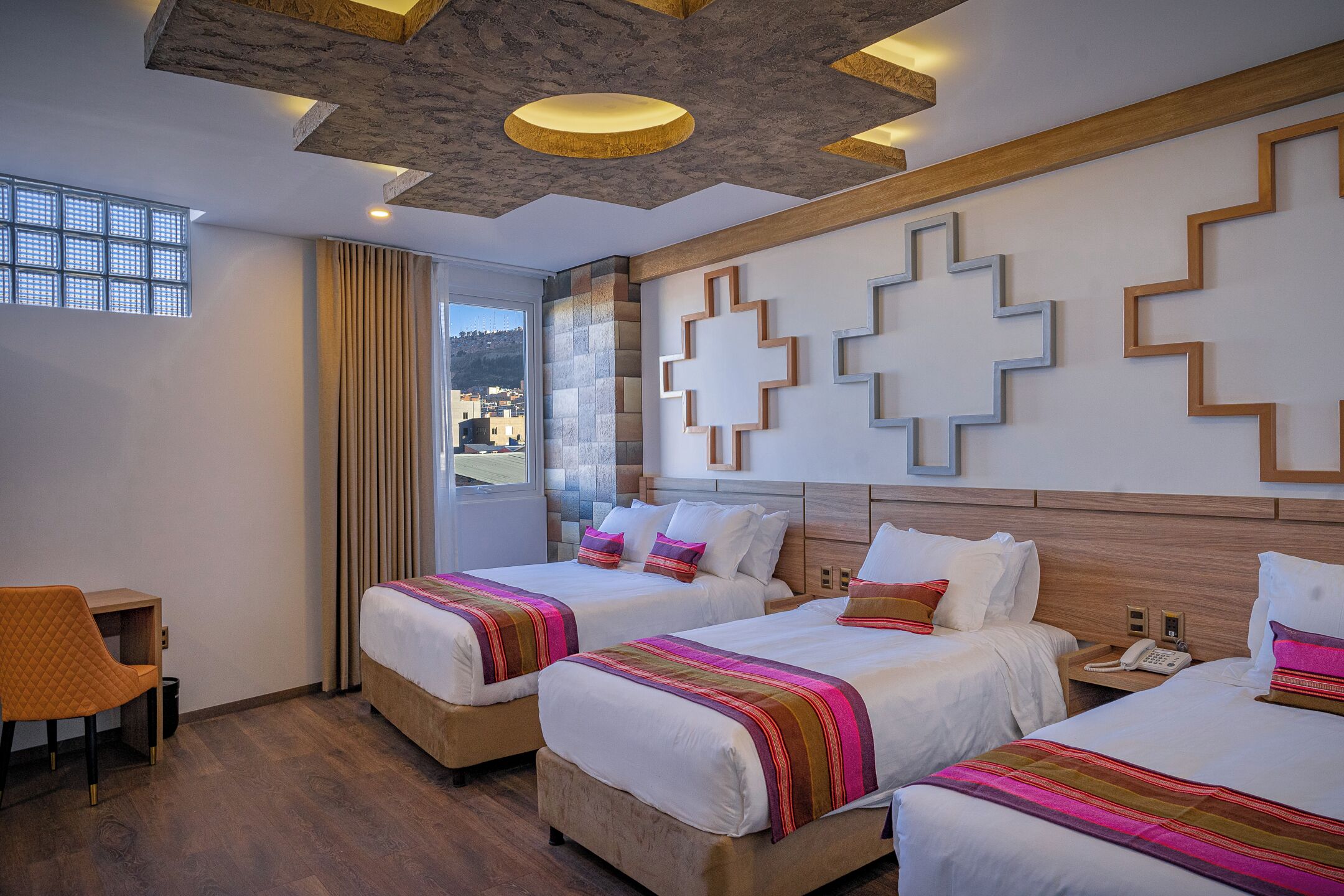 A hotel room with two beds, a desk, and a view of the outside.