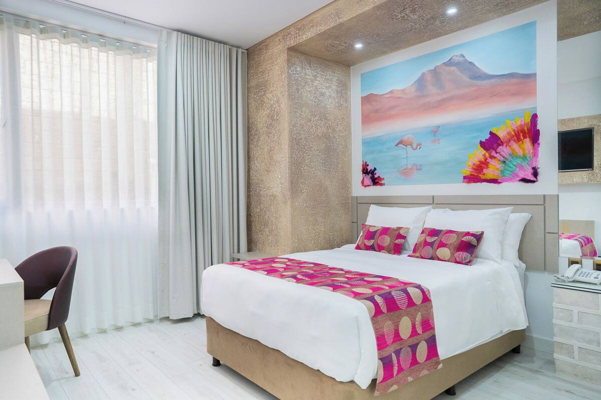 Quarto de hotel com uma cama grande, uma escrivaninha e um quadro na parede.