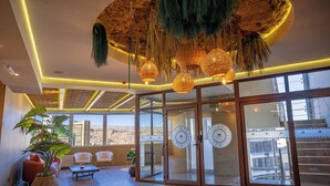 Ein geräumiger Wohnbereich mit einer großen Glasschiebetür, die auf einen Balkon führt, einer Decke mit hängenden Lampen aus Bast und einer üppigen Topfpflanze.