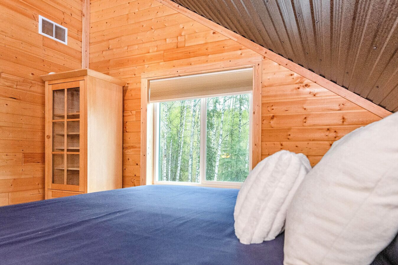 Una habitación de cabaña de madera con una cama, una ventana con vistas al bosque y un armario de madera.