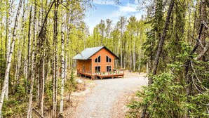 A cabin with a deck, surrounded by a forest.
