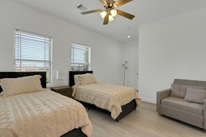 A bedroom with two beds, a ceiling fan, and a grey sofa. - The Krakow | Sleeps 16 (Houston)