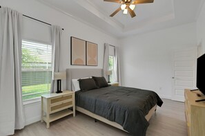 Un dormitorio con cama, mesitas de noche, ventilador de techo y una puerta.