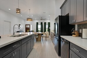 A modern kitchen with a central island, dark cabinetry, and a black refrigerator. - The Krakow | Sleeps 16 (Houston)