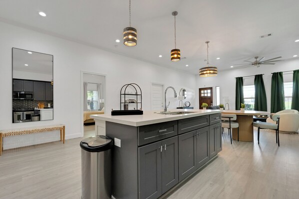 A modern kitchen with a central island, overhead pendant lights, and a ceiling fan. - The Krakow | Sleeps 16 (Houston)