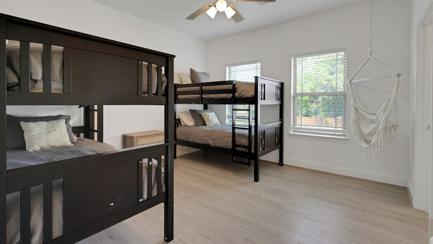 A room with two bunk beds, a ceiling fan, and a window with blinds. - The Krakow | Sleeps 16 (Houston)