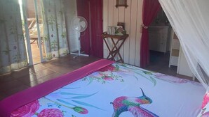 A bedroom with a bed, a fan, a small table, and a window with curtains. - Villa Manguier, a heavenly vacation!
Swimming pool, sea view, car rental (Rivière-Salée)