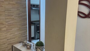 Una sala de estar moderna con una pared de piedra, una consola blanca con objetos decorativos, una planta verde grande y un reposapiés rojo.