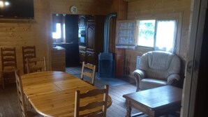 Een houten blokhut van binnen, met een eettafel, stoelen, een bank en een keuken met kastjes en een fornuis.