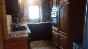 Een kleine keuken met houten kastjes, een gasfornuis, een spoelbak en een raam dat natuurlijk licht binnenlaat.