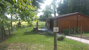 Een houten hut met een veranda, omgeven door een omheinde tuin met een pad er naartoe.