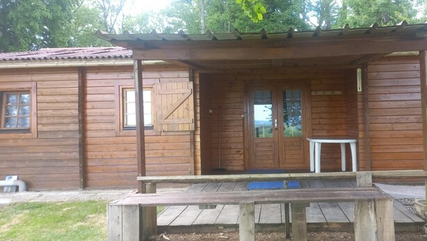 Een houten blokhut met een overdekte veranda, één raam en een kleine tafel.
