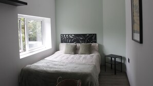 A bedroom with a bed, a small table, a window, and a headboard with a leaf design. - Modern en-suit room in bristol 4 (Bristol)