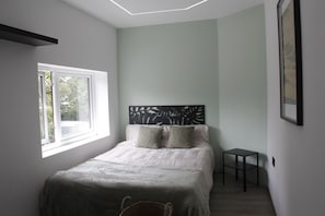 A bedroom with a bed, a small table, a window, and a headboard with a leaf design.