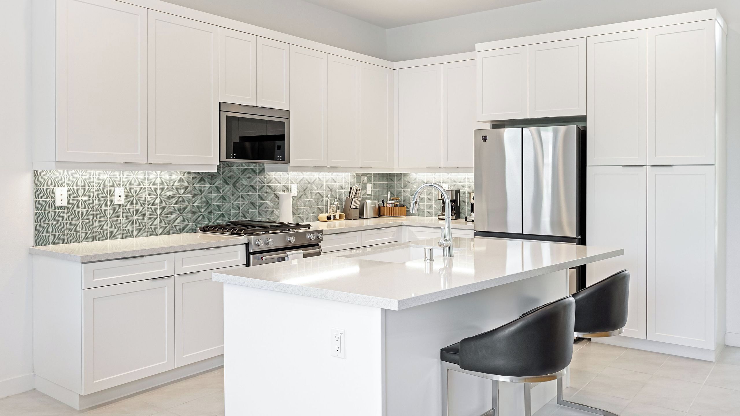 A modern kitchen with white cabinetry, a stainless steel refrigerator, a gas stove, and a tiled backsplash.