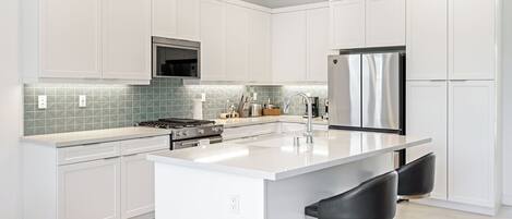 A modern kitchen with white cabinetry, a stainless steel refrigerator, a gas stove, and a tiled backsplash.