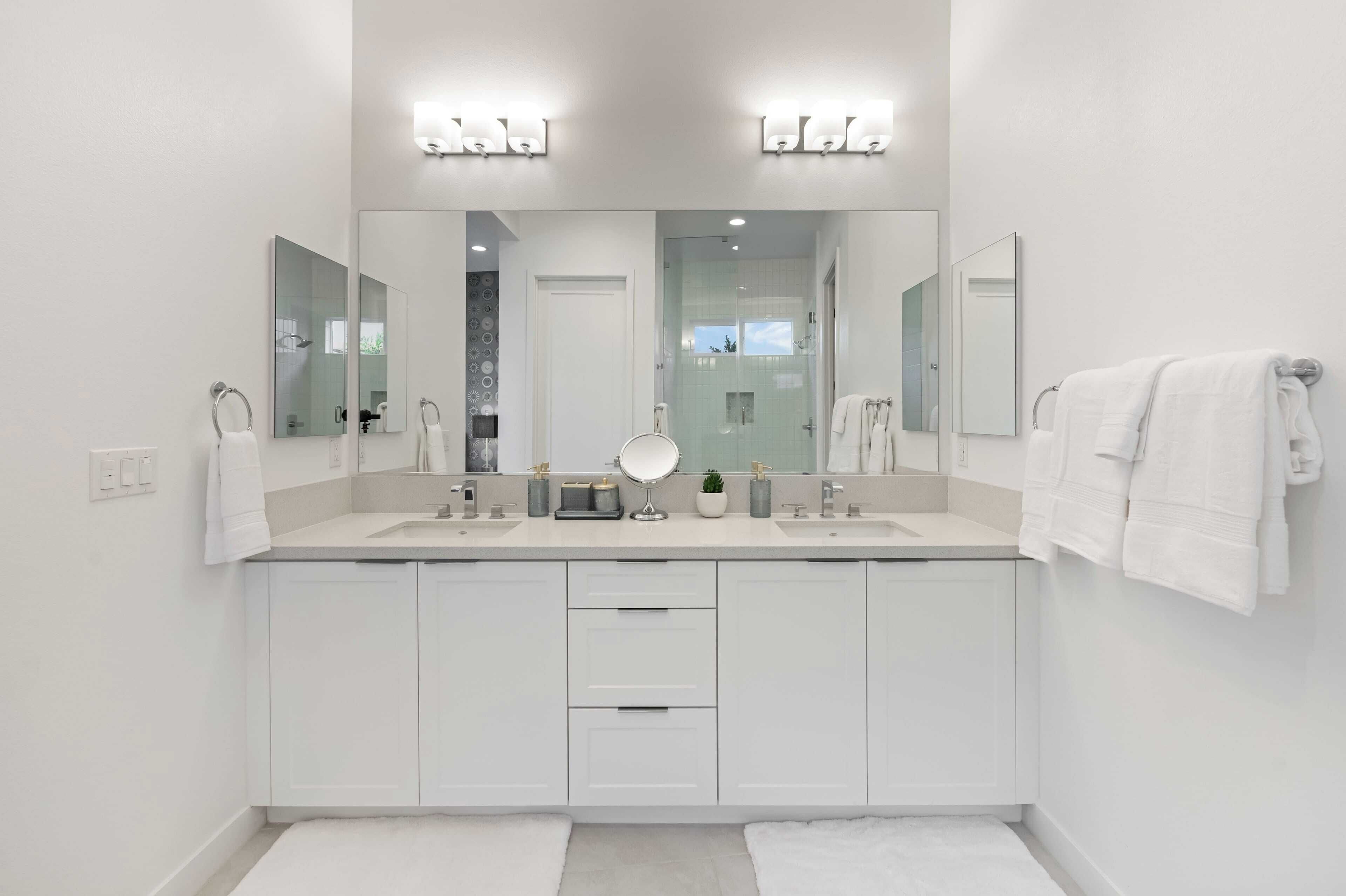 A modern bathroom with two sinks, a large mirror, and white cabinetry.