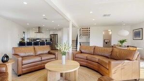 A modern living room with leather sofas, a wooden coffee table, and a kitchen in the background.