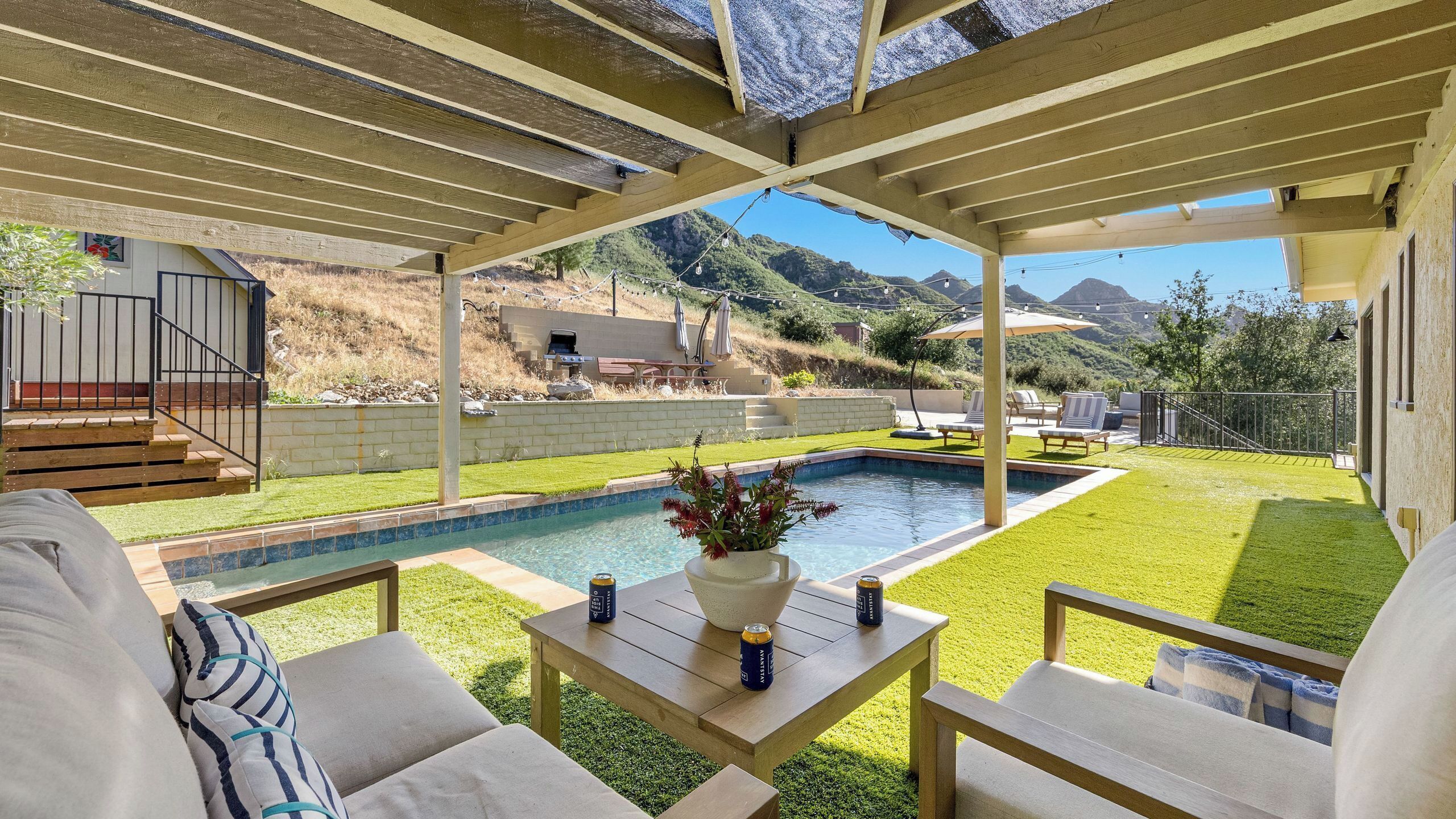Eine überdachte Terrasse mit Pool, Gartenmöbeln und Blick auf eine Berglandschaft.