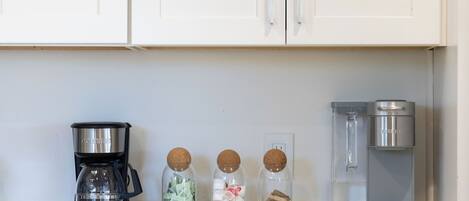 Una encimera de cocina con una cafetera, tres frascos de especias y un dispensador de agua.
