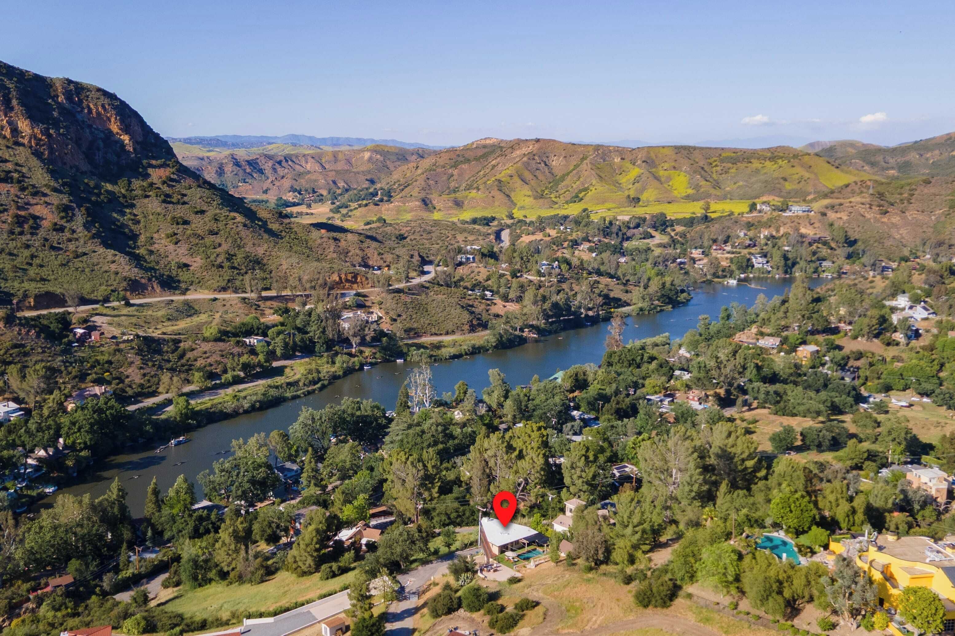 A mountainous landscape with a river, houses, and a red marker indicating a specific location.