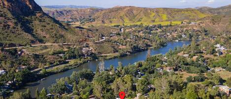 A mountainous landscape with a river, houses, and a red marker indicating a specific location.
