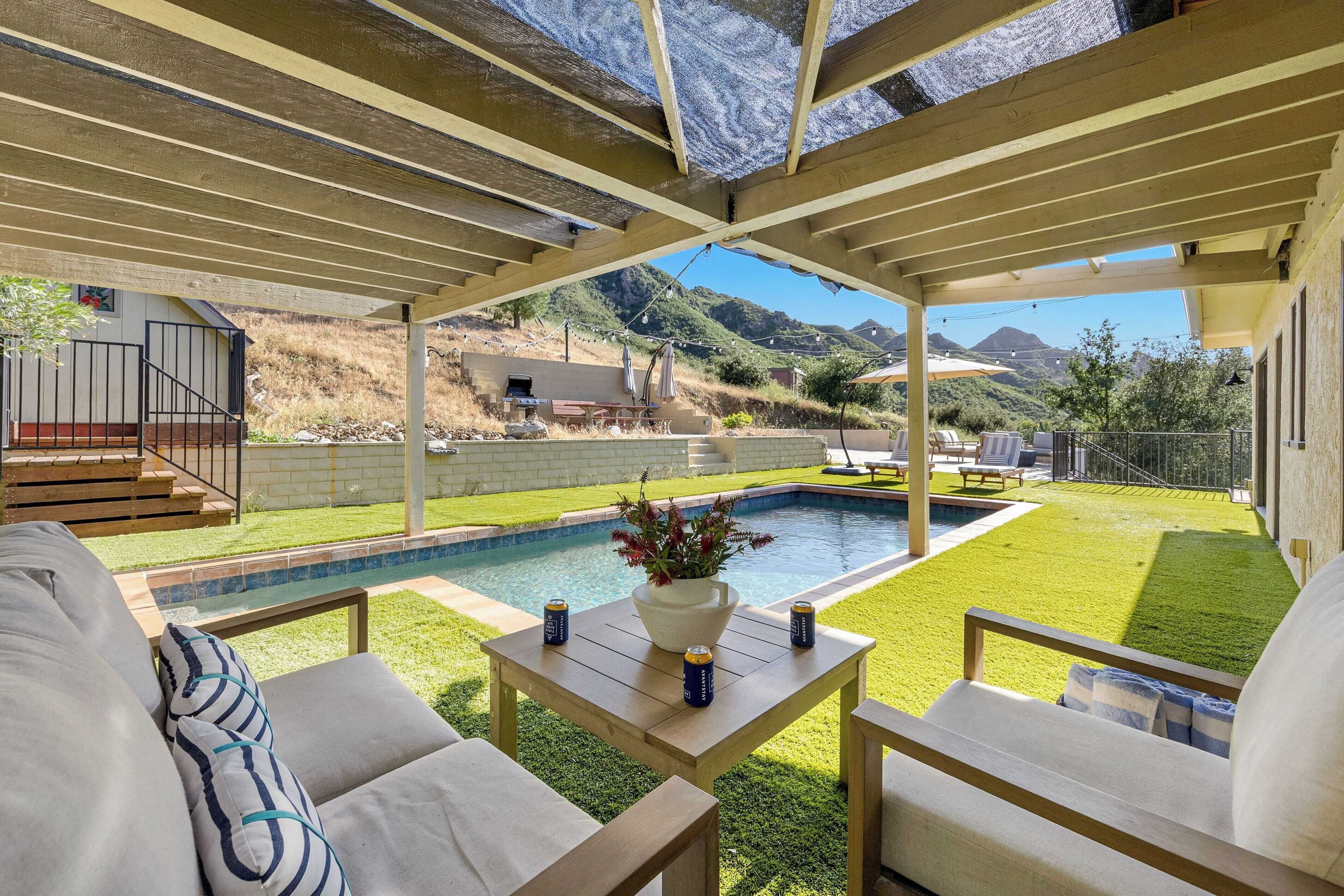 A covered patio with a pool, outdoor furniture, and a view of the surrounding landscape.