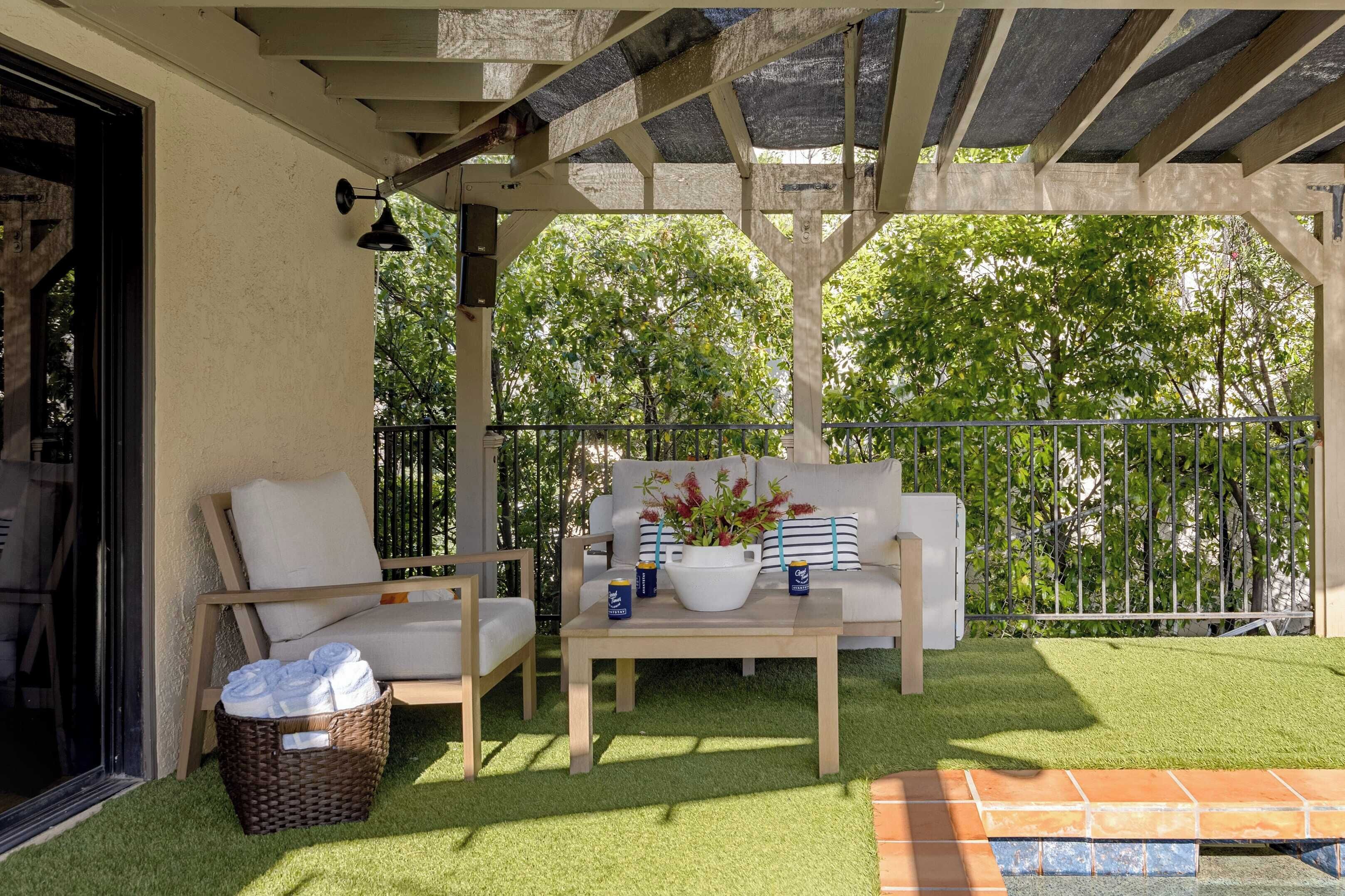 A covered outdoor seating area with a sofa, chairs, and a table with a potted plant.