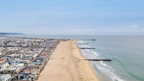 A coastal cityscape with a long beach, a pier extending into the ocean, and residential buildings along the shore.