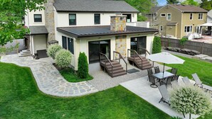 Une maison moderne avec une façade en pierre, un patio couvert et une pelouse bien entretenue.