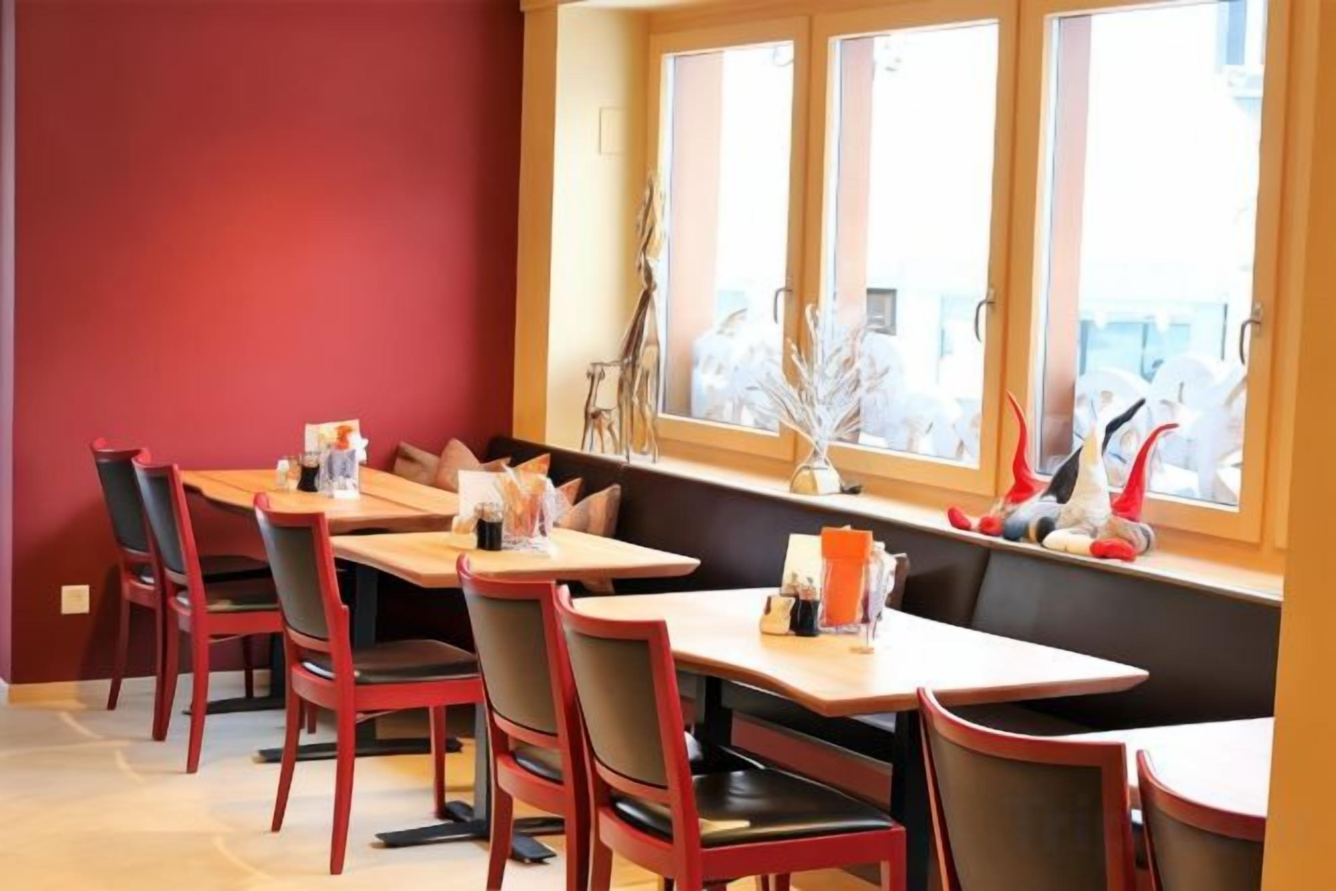 A dining area with multiple tables and chairs, a window with decorative items, and a red wall.