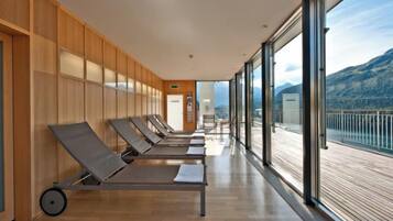 A row of sun loungers on a balcony with a view of mountains.