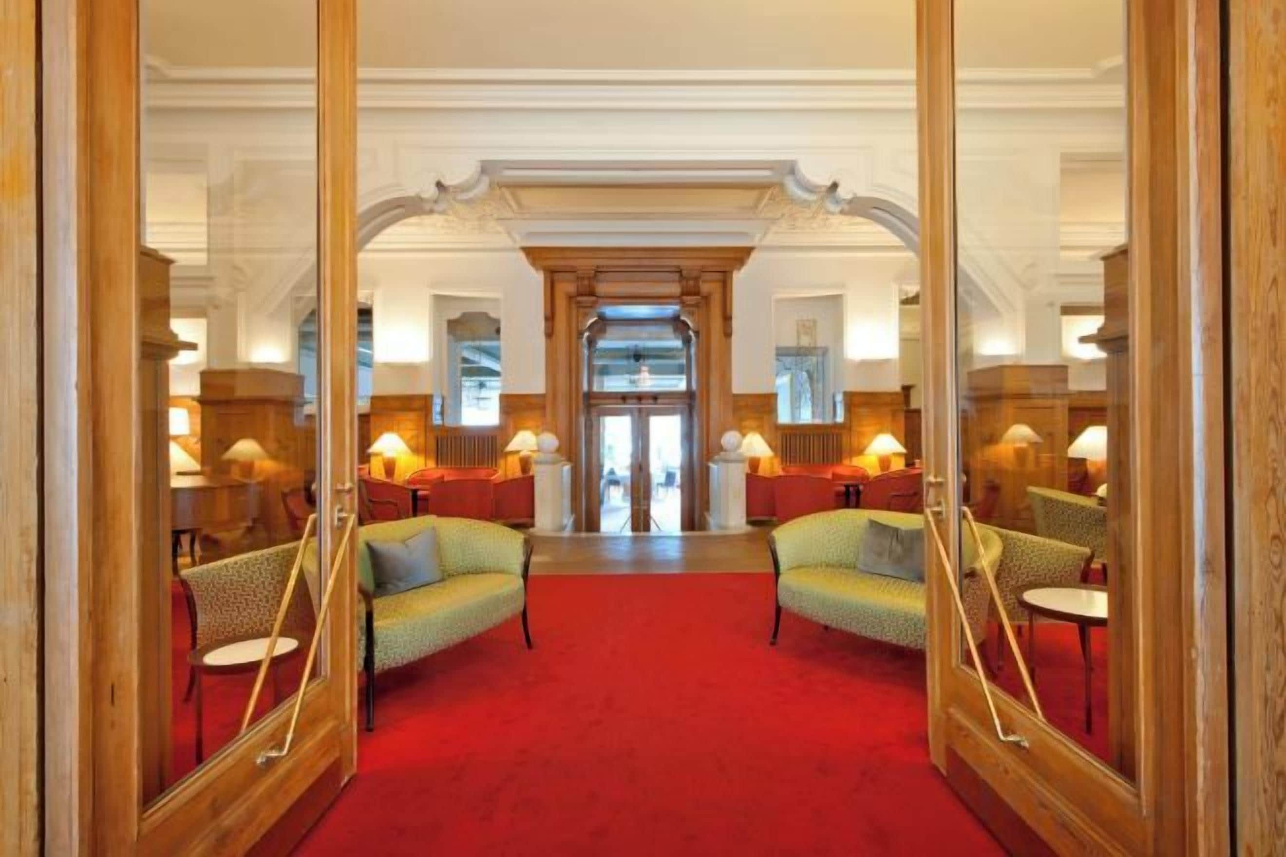 Eine Hotelhalle mit rotem Teppich, Holzmöbeln und einer Spiegelwand, die den Raum widerspiegelt.