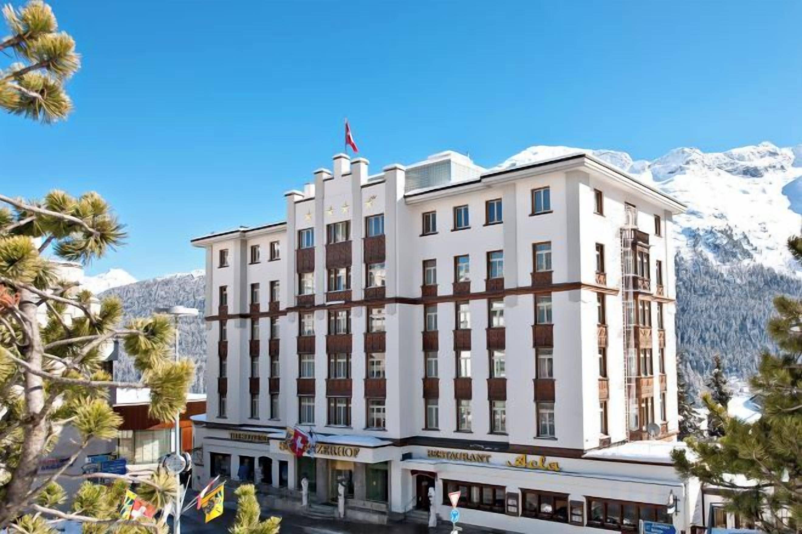A multi-story hotel with a prominent entrance, flags, and a mountain backdrop.