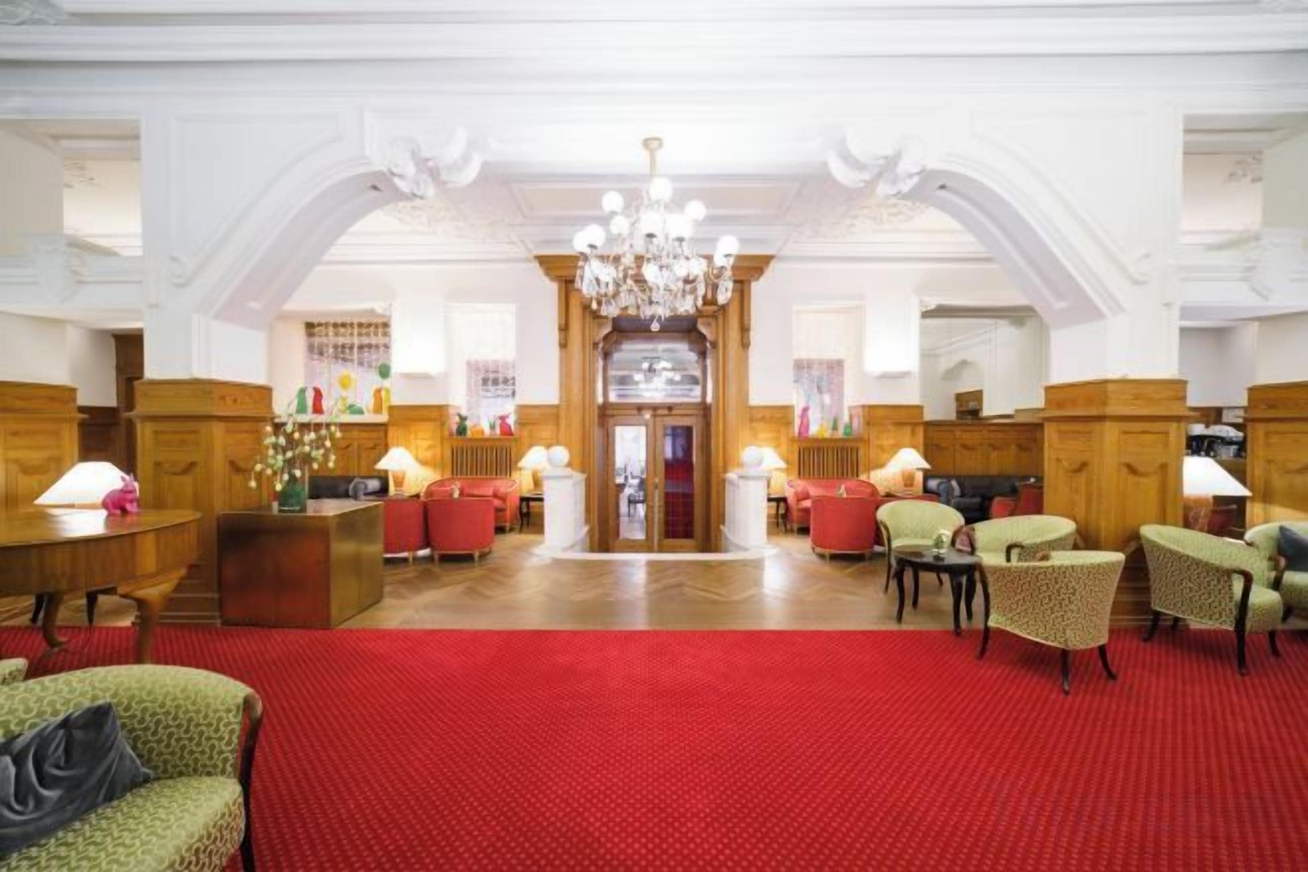 A hotel lobby with a red carpet, wooden furniture, and a chandelier.