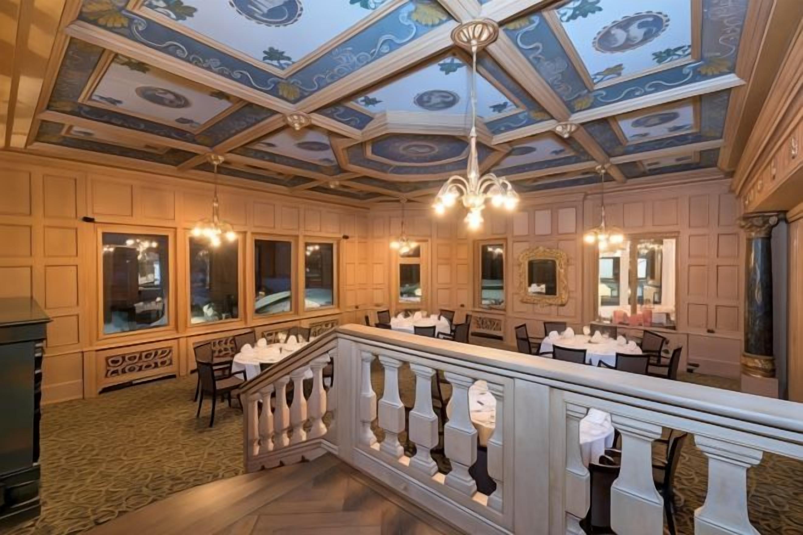 A hotel dining area with a high ceiling, chandeliers, and a balcony with a railing.