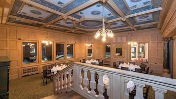 A hotel dining area with a high ceiling, chandeliers, and a balcony with a railing.