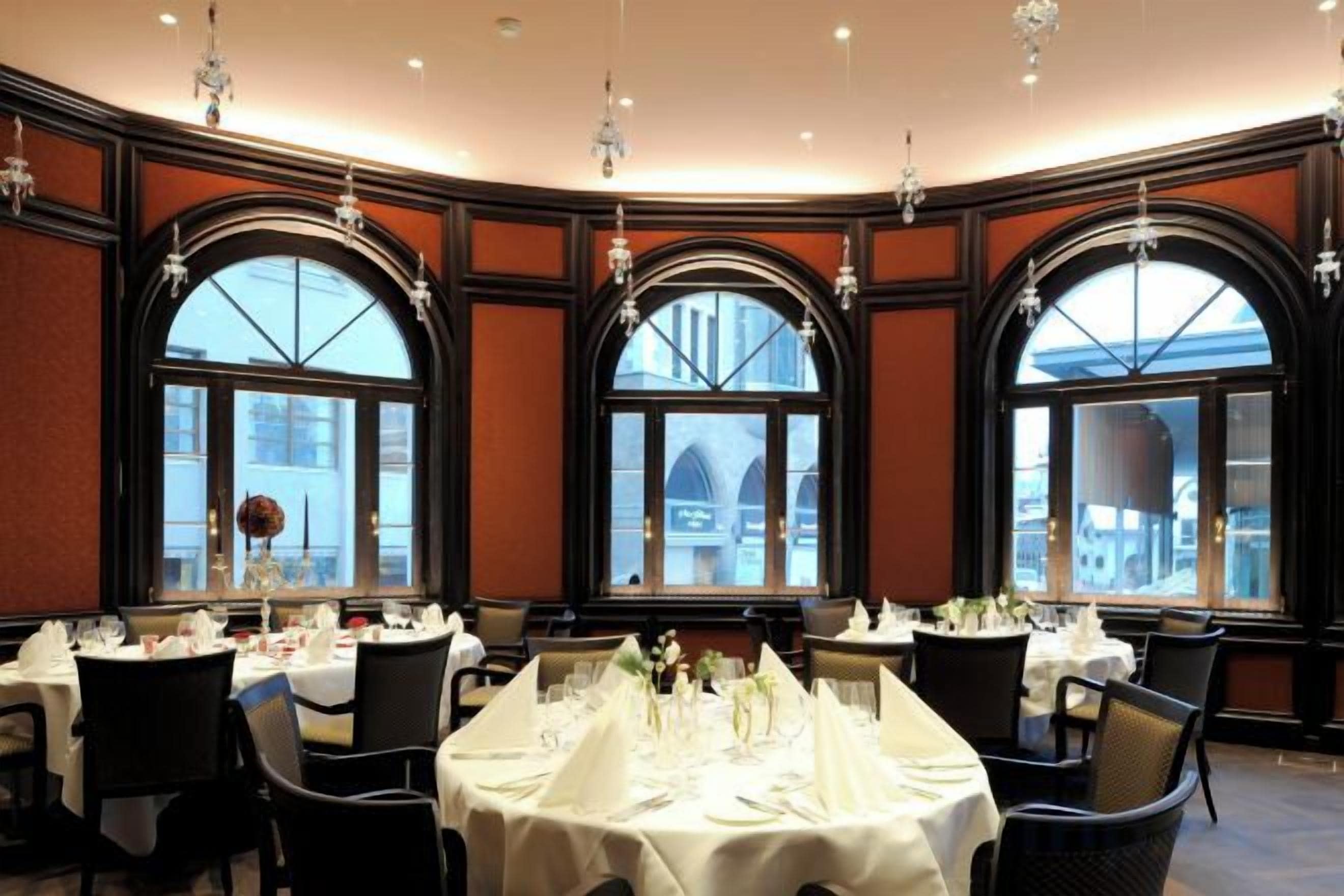 A dining area with tables set for service, large windows with arched tops, and hanging light fixtures.
