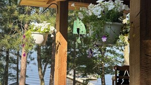 A wooden deck with hanging flower planters and a bench. - Charming 3-bedroom cabin with WiFi, AC in lovely Eagle River sleeps 8 people. (Eagle River)