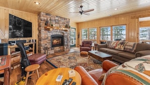 A cozy cabin interior with a stone fireplace, wooden walls, a large TV, and a comfortable seating area. - Charming 3-bedroom cabin with WiFi, AC in lovely Eagle River sleeps 8 people. (Eagle River)