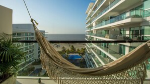 Un hamac sur un balcon donnant sur une plage, avec des bâtiments modernes en arrière-plan.