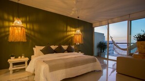 Une chambre avec un grand lit, deux lampes suspendues, une vue sur l’extérieur et un hamac.