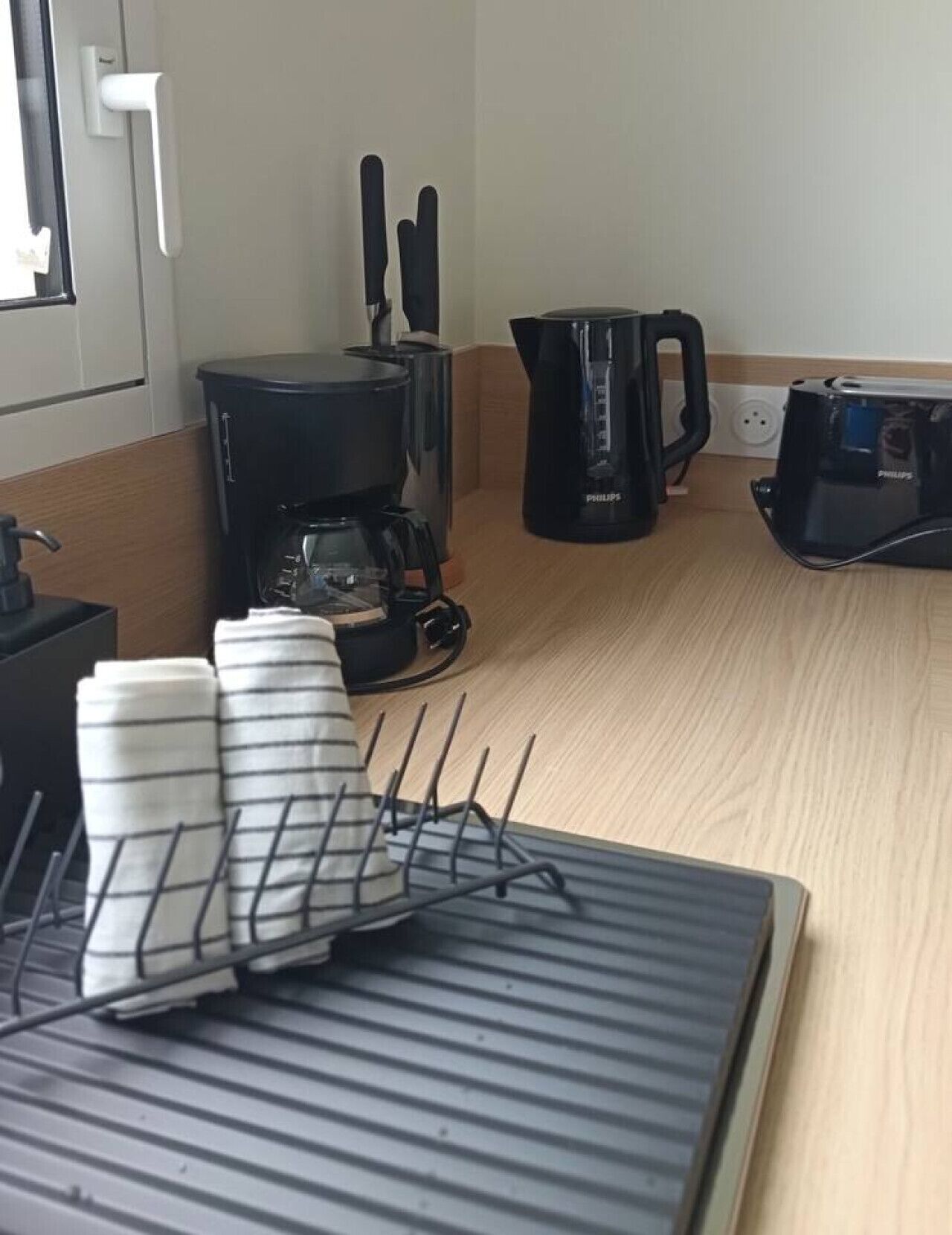 Una cocina con cafetera, hervidor y tostadora. Toallas a rayas en un escurreplatos.
