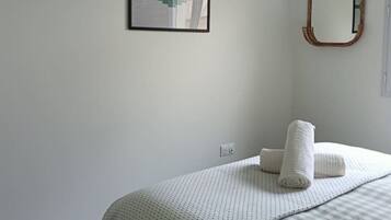 Une chambre à coucher avec un lit, un oreiller, un miroir fixé au mur et un tableau encadré.