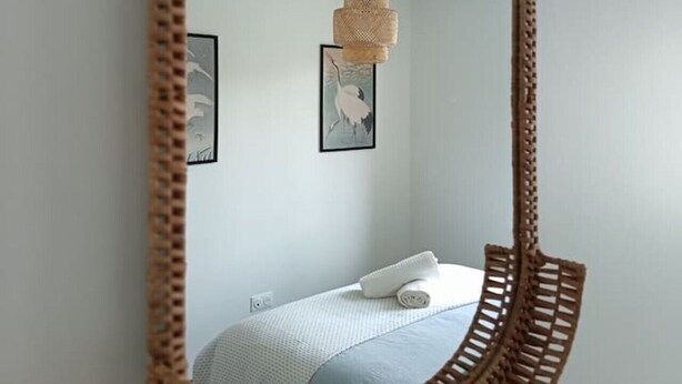 Un miroir doté d’un cadre tressé qui reflète un lit, un luminaire suspendu et deux tableaux encadrés accrochés au mur.
