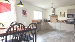 Une cuisine moderne avec un coin repas, comprenant une table et des chaises en bois, un parasol rouge et une grande fenêtre.