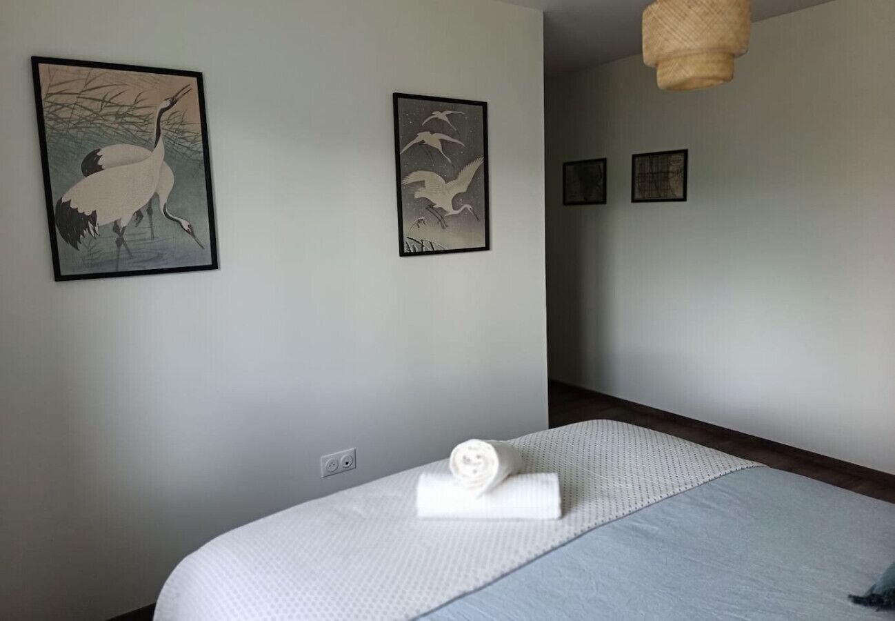 A hotel room with a bed, a rolled towel, and two framed artworks on the wall.
