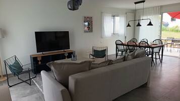 Un salon moderne comprenant un grand canapé, un téléviseur, un coin repas avec des chaises et une table.